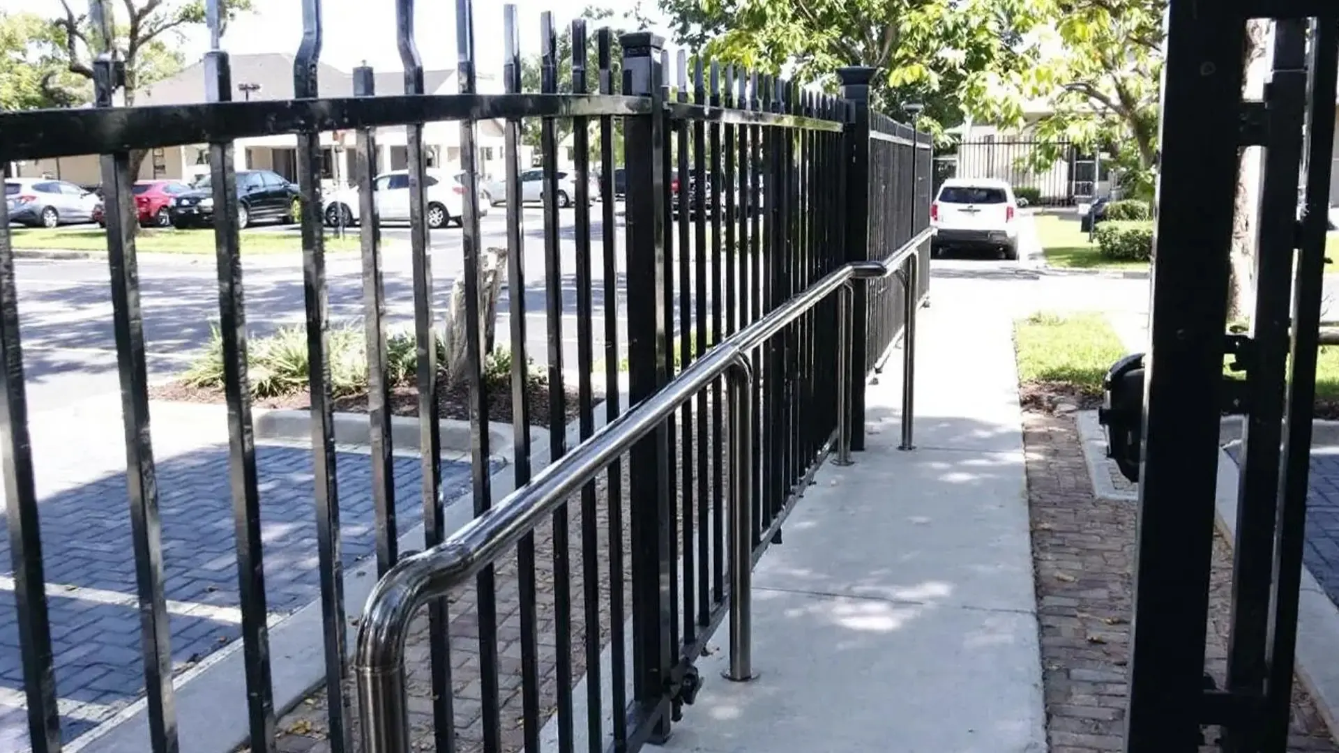 A black aluminum fence runs alongside an accessibility ramp equipped with stainless steel handrails. The design combines functionality and security, providing a safe, ADA-compliant entryway for pedestrians while maintaining a clean, professional appearance.